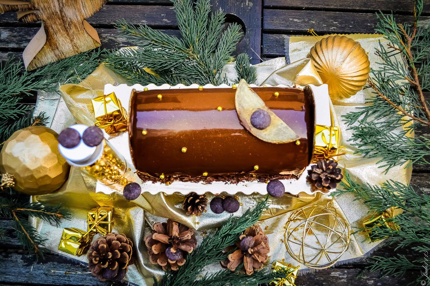 Photo d’une bûche de Noël entourée de pommes de pin, de feuilles et de décorations de Noël.