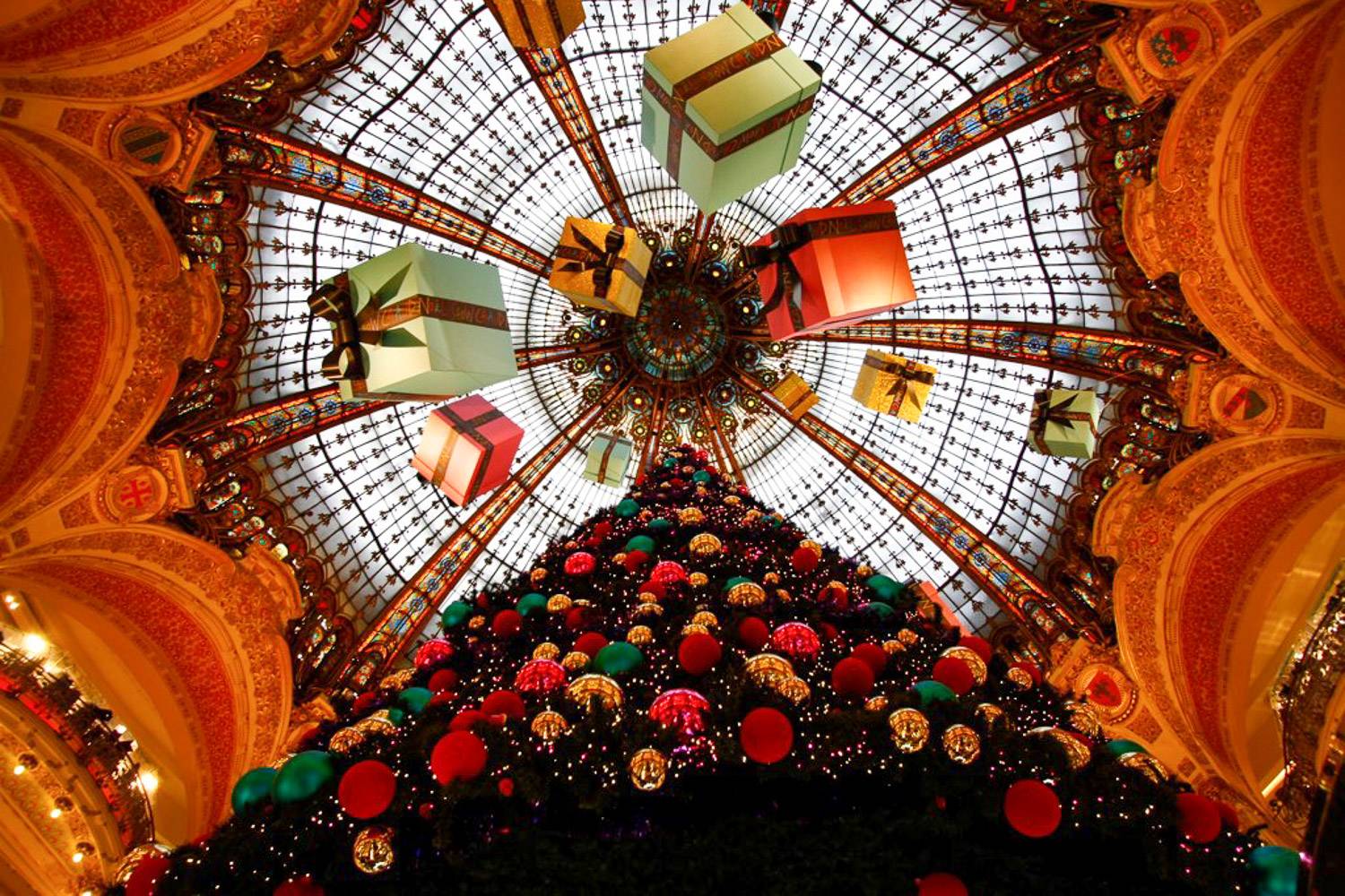 Photo de la coupole en verre du magasin principal des Galeries Lafayette, avec un imposant sapin de Noël et des cadeaux suspendus au dôme.