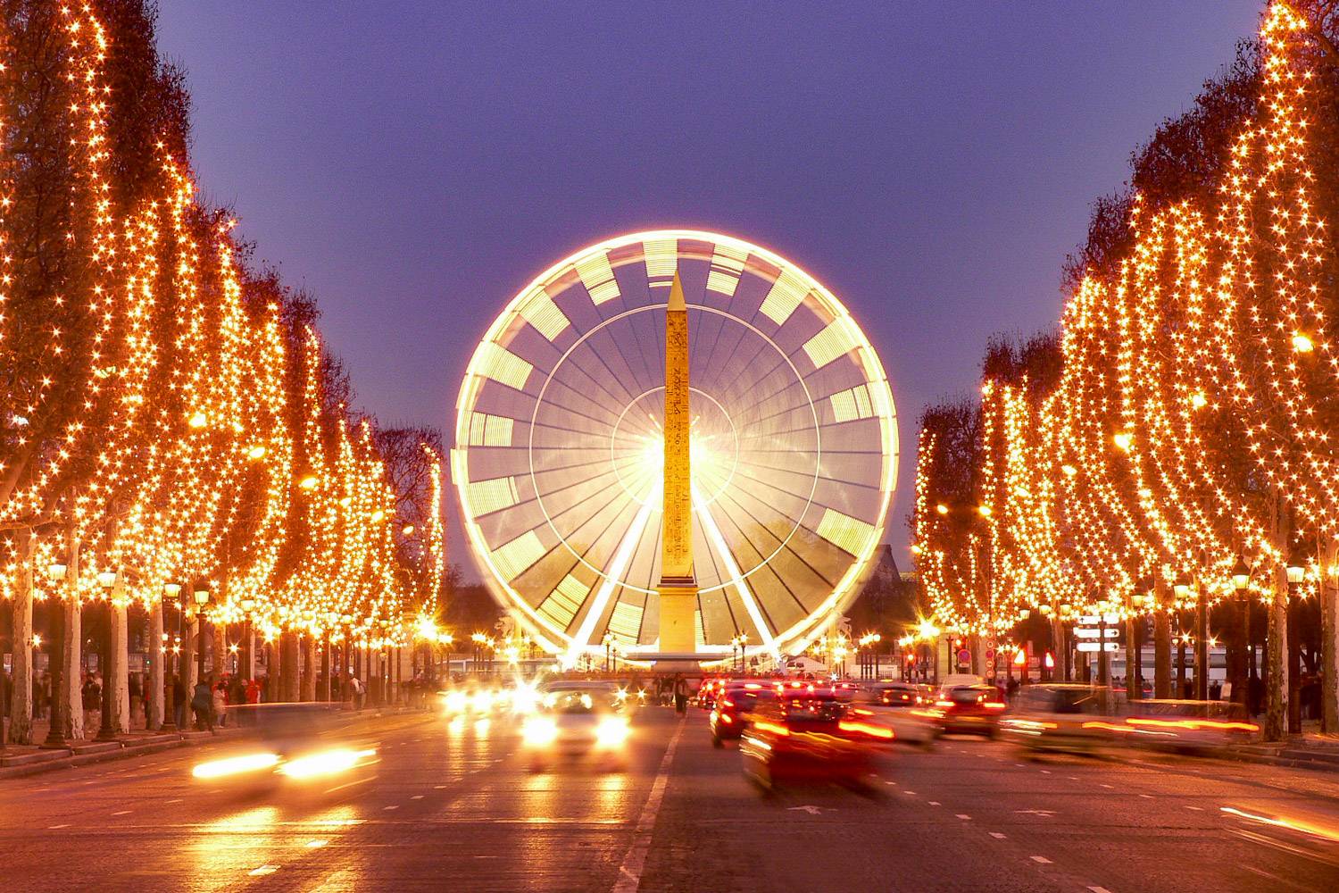 Photo de l’avenue des Champs-Elysées avec des sapins décorés pour Noël bordant les deux côtés de l’avenue, avec une grande roue au centre.