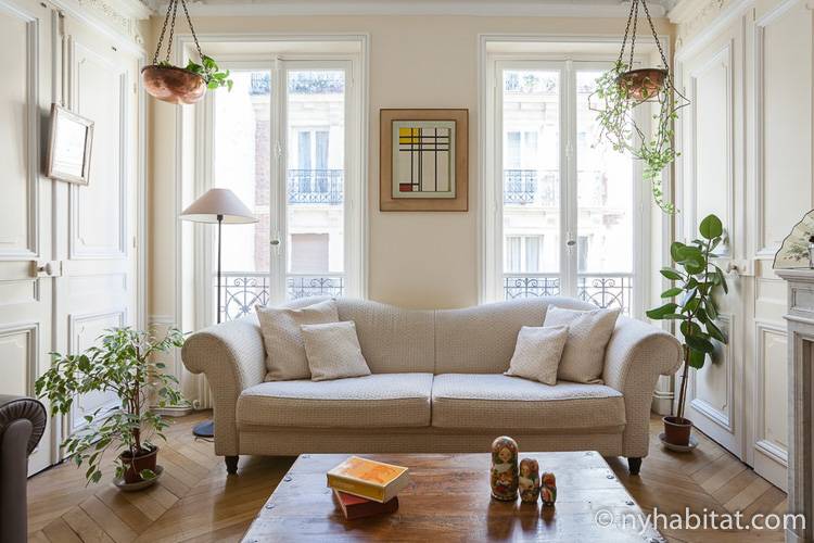 Photo du salon de la location de vacances PA-4729 avec un élégant canapé blanc au premier plan et deux portes menant au balcon à l’arrière.