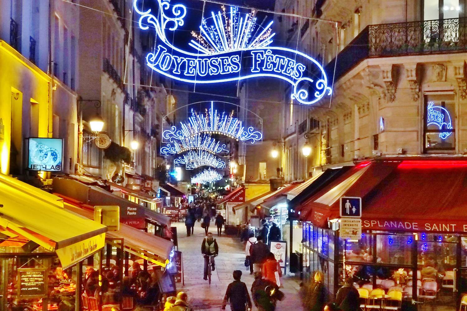 Photo de la rue Montorgueil avec des boutiques de chaque côté et des décorations de Noël illuminant la rue.