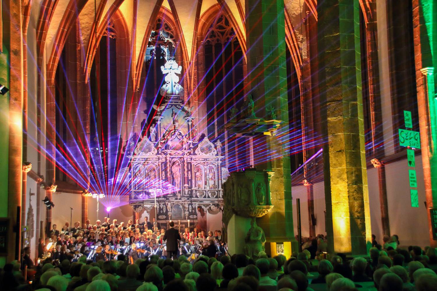 Photo de la Sainte-Chapelle pendant un concert, avec des lumières colorées brillant de la scène en direction du public.