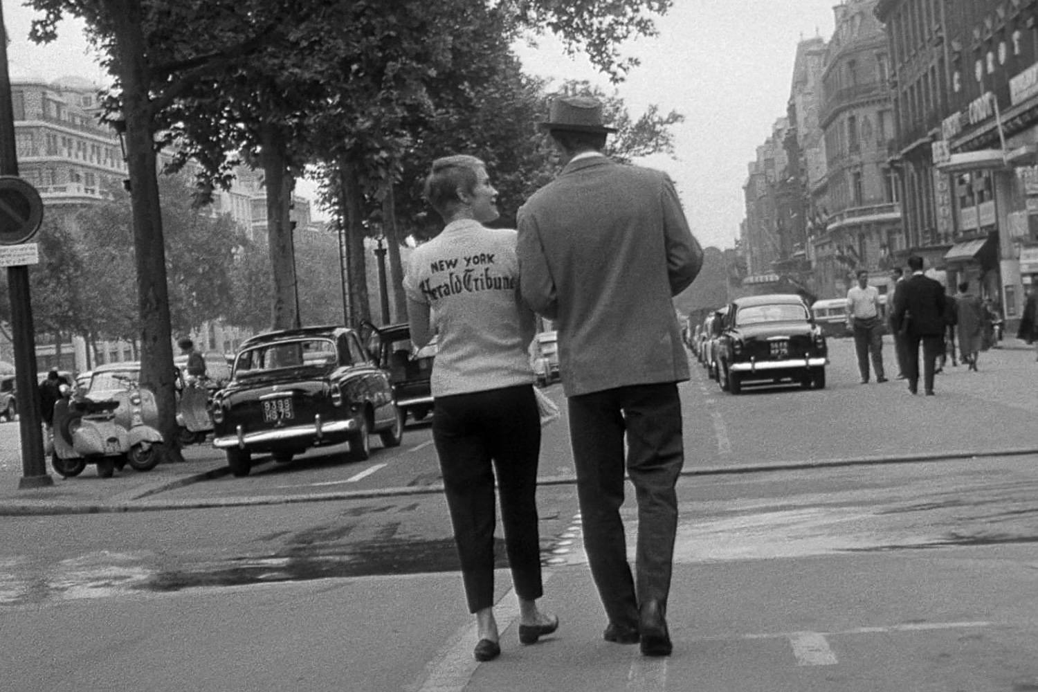 Image en noir et blanc d’un couple marchant sur les Champs Élysées à Paris, extraite du film de Jean-Luc Godard “À bout de souffle”