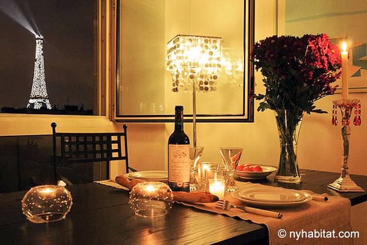 Image d'une table à manger avec des bougies, une bouteille de vin et des roses avec vue sur la Tour Eiffel par la fenêtre