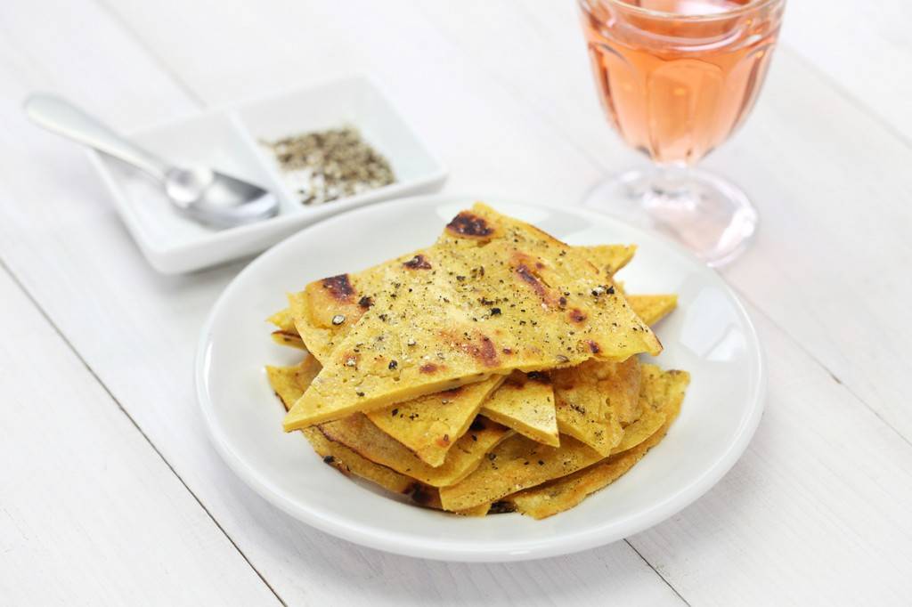 Immagine di un piatto con fette di socca, sale e pepe e un bicchiere di vino rosato