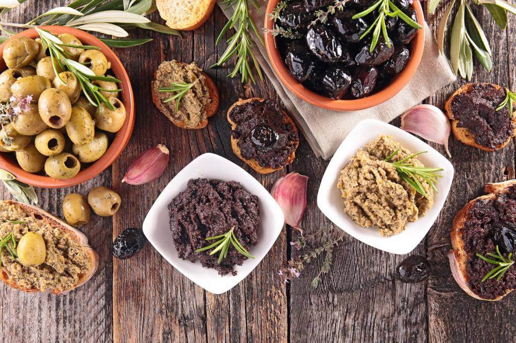 Immagine di diversi tipi di olive e tapenade disposti su un tavolo