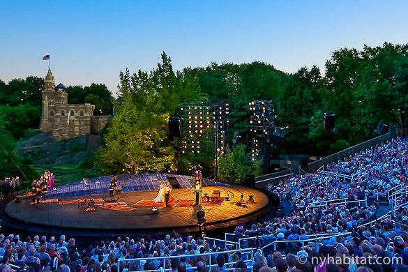 Foto di persone che assistono a una rappresentazione teatrale di Shakespeare all'aperto con castello sullo sfondo
