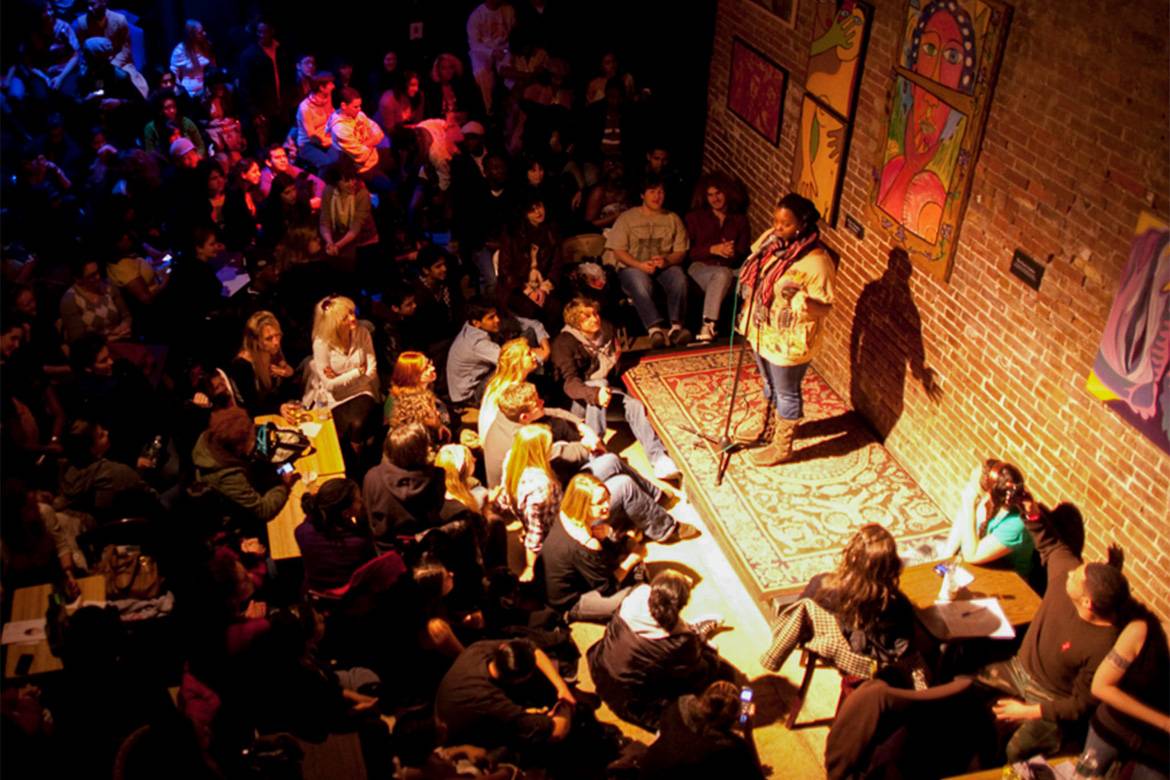 Immagine di una persona su palco in penombra in una serata di poesia