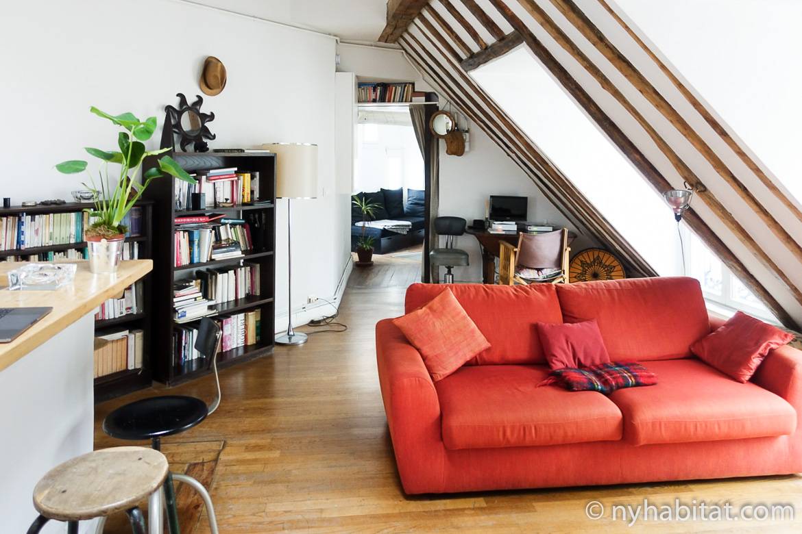 Immagine del soggiorno di PA-3780 con divano rosso, librerie e soffitto con travi a vista.