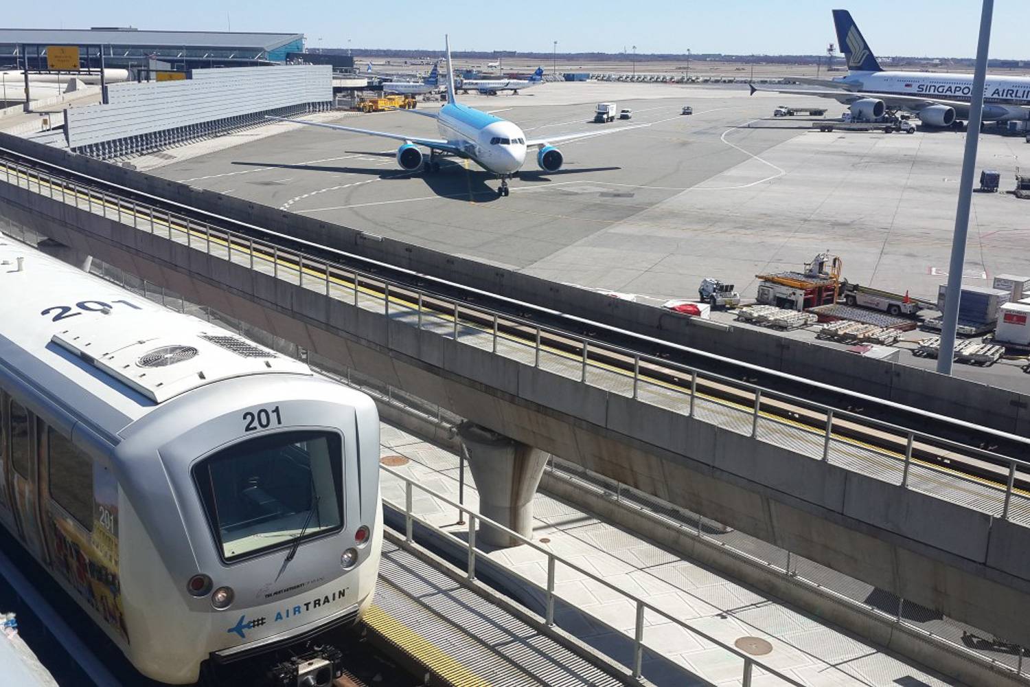 Immagine dell’AirTrain di JFK che viaggia tra i terminal con gli aeroplani sull’asfalto nello sfondo.