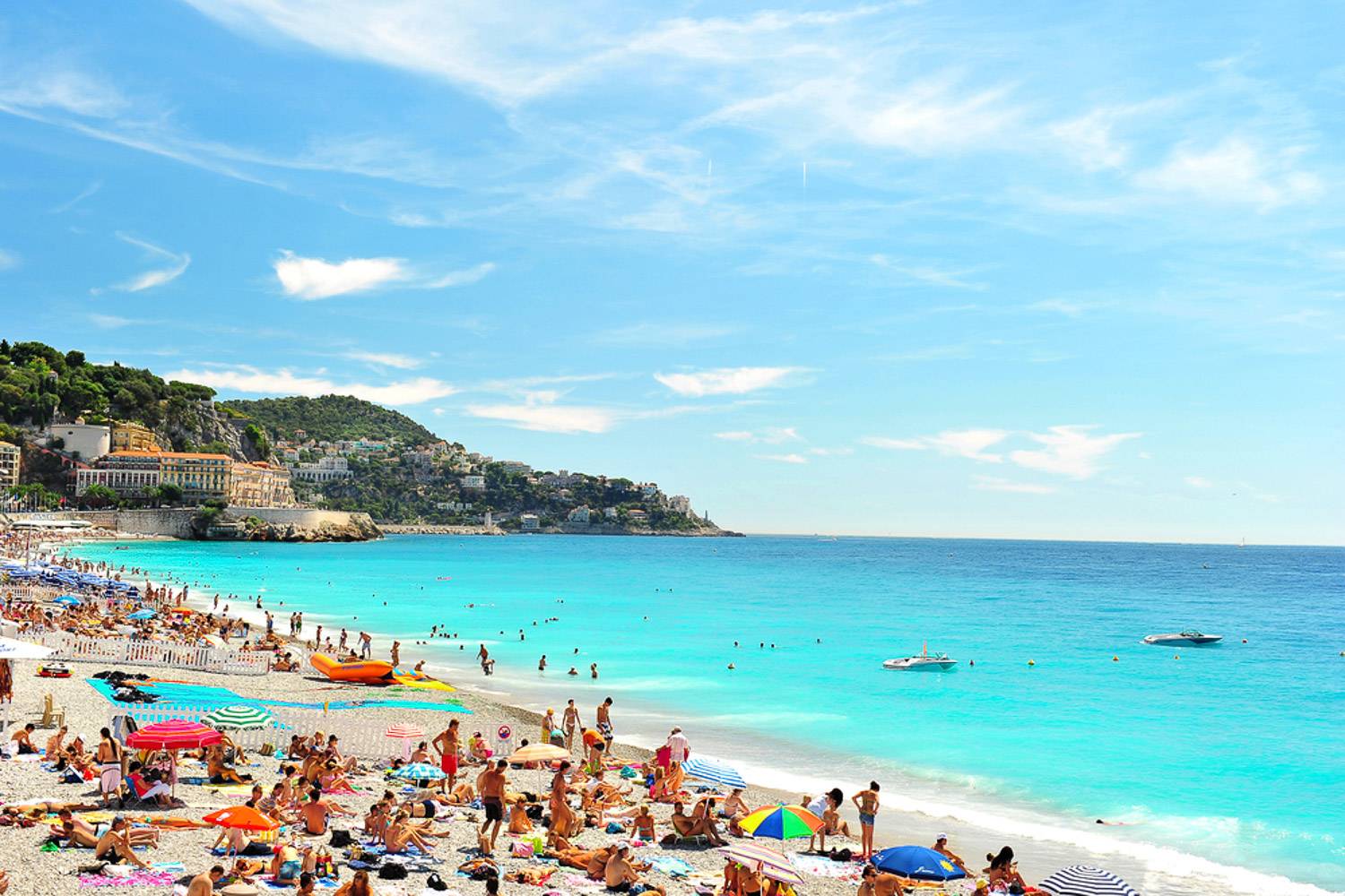 Immagine di una spiaggia di Nizza con persone sulla sabbia e barche in acqua.