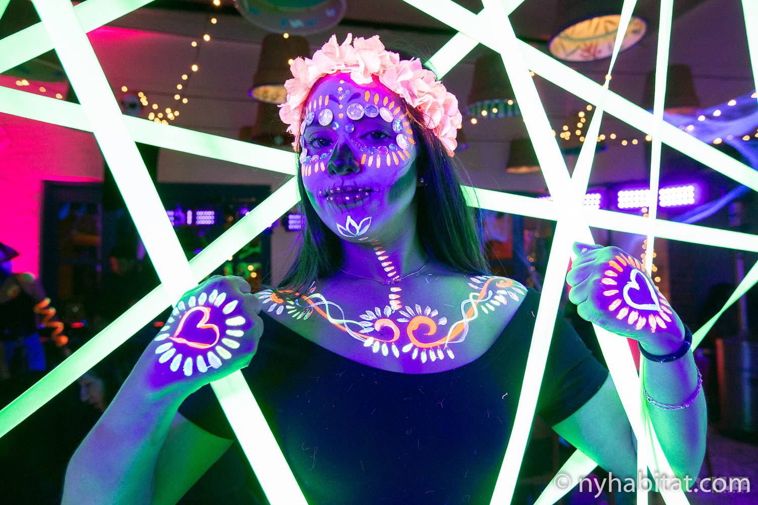 Immagine di una donna avvolta da luci al neon con corpo e volto dipinti con colori fosforescenti.