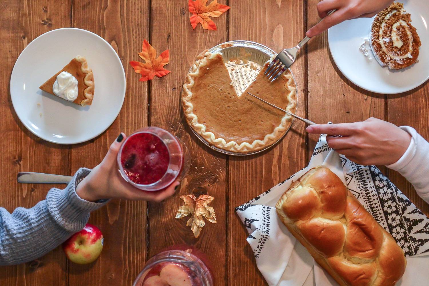 Immagine di una vista dall’alto di un tavolo da pranzo addobbato con torte, vin brulé, pane challah e mele.