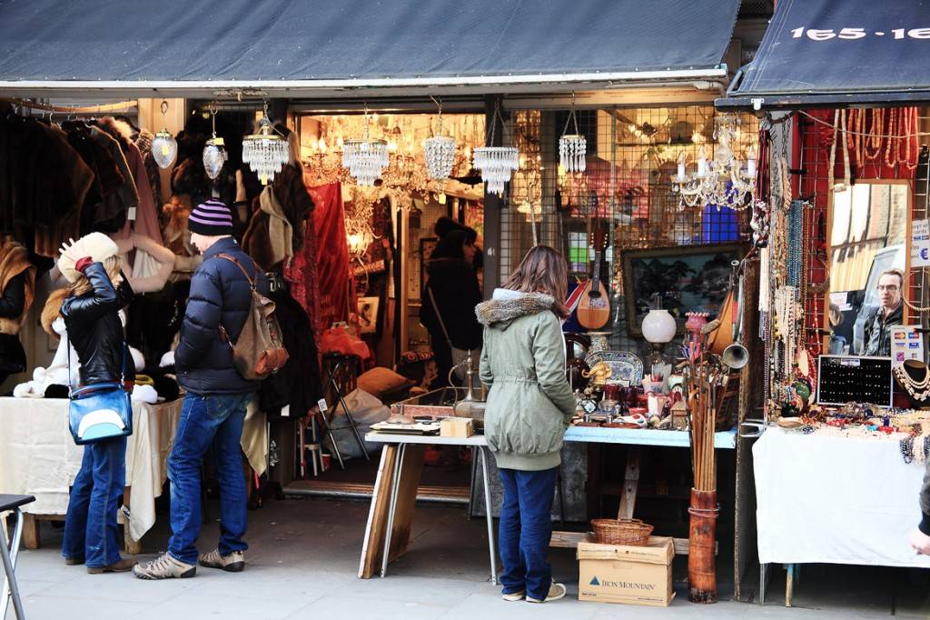 Imagen de visitantes curioseando los puestos de antigüedades del mercado de Portobello Road, donde están expuestos numerosos objetos