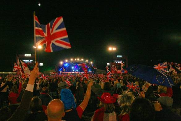 Fotografía del público disfrutando de un concierto al aire libre y agitando banderas británicas