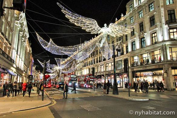 Imagen de una calle comercial con autobuses de dos pisos y luces de Navidad en forma de ángel.