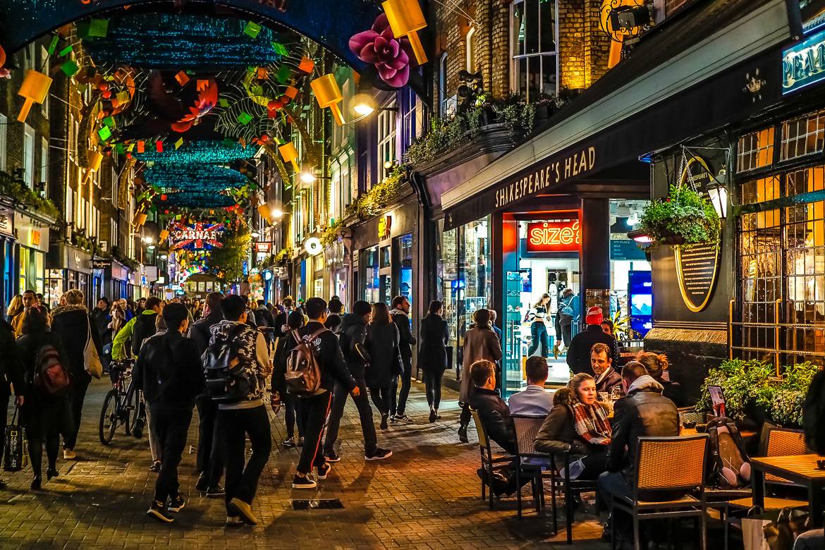 Imagen nocturna de las luces y peatones de compras, con un cartel que pone “Carnaby Street Carnival” en SoHo, Londres