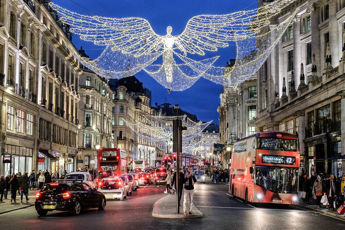 Imagen de las luces de Navidad con motivos de ángeles decorando una calle por la que circulan autobuses rojos de dos plantas