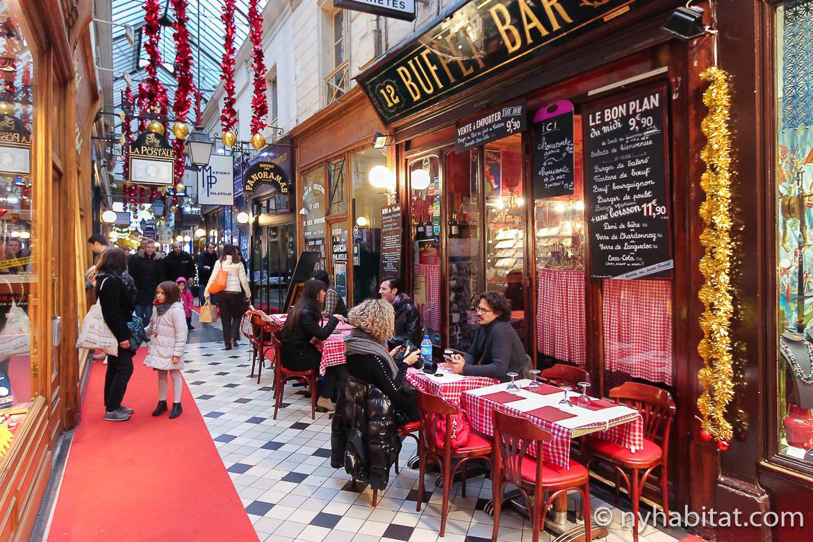 imagen de gente comiendo dentro de la galería comercial Passage du Panorama con techo de cristal y decoración navideña
