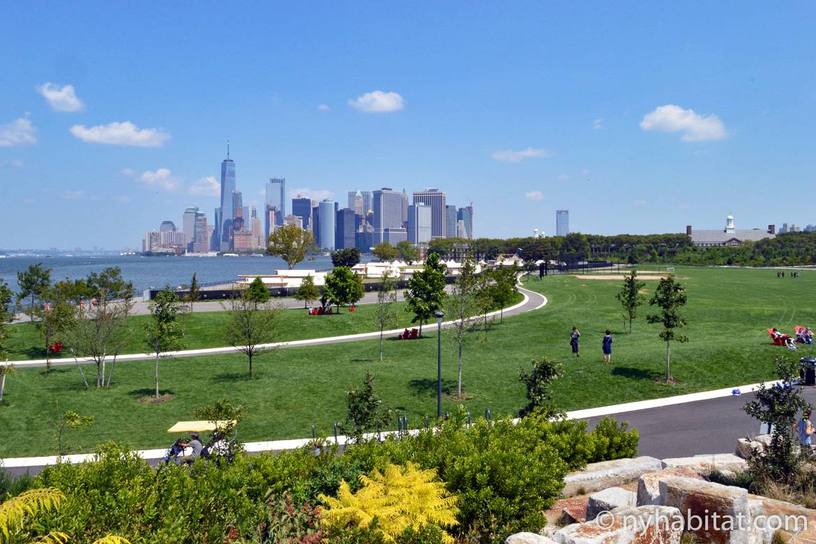 Imagen de una zona de césped y senderos en Governor’s Island con el skyline de Manhattan al fondo.