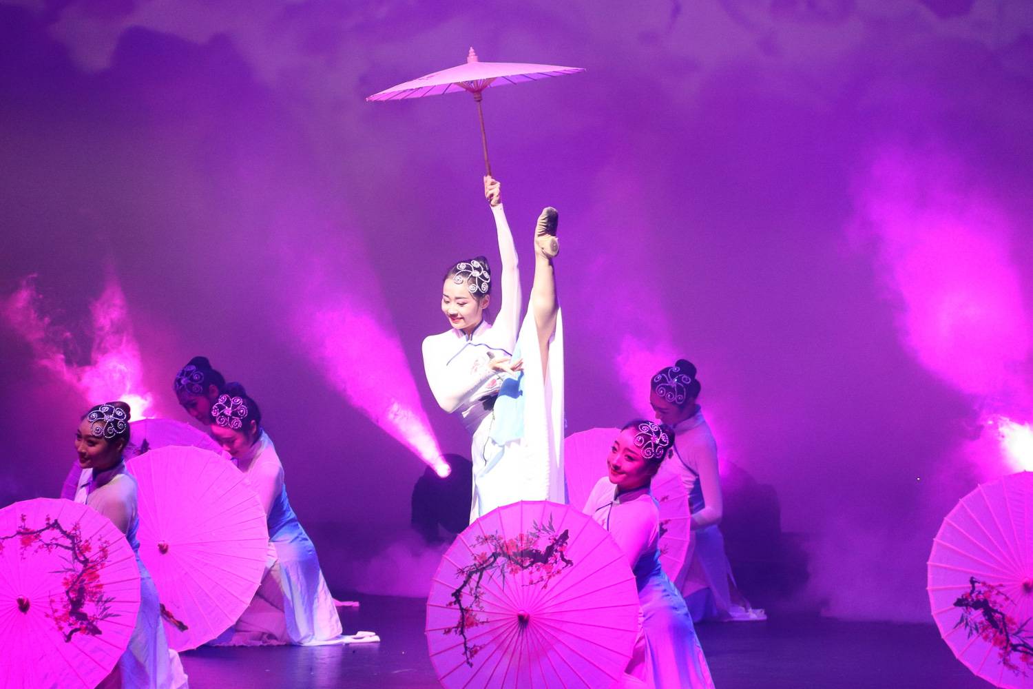Imagen de una bailarina asiática con la pierna levantada, sosteniendo una sombrilla y con iluminación morada
